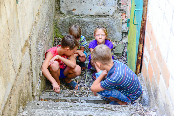 Bodrum katında çocuklar, üç erkek ve bir kız demir kapının yanında dış dünyadan basamaklarda saklanıyorlar. Post-Prodüksiyon fotoğraf. - Fotoğraf, Görsel