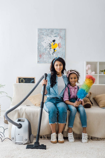 attractive african american woman sitting on sofa near adorable daughter  - Fotó, kép