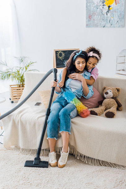 adorabile bambino afroamericano che abbraccia la madre stanca seduta sul divano
  - Foto, immagini