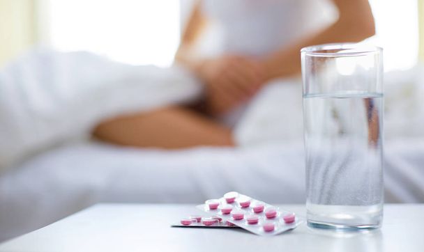 Young beautiful woman with pills lying on bed in bedroom - 写真・画像