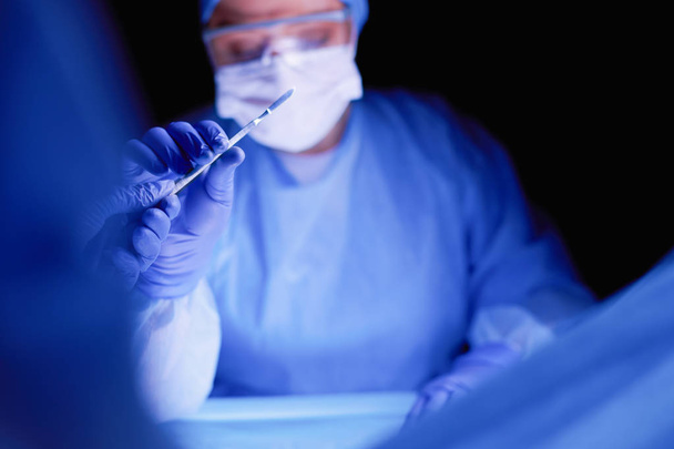 Doctor performing surgery in a dark background. - Foto, Imagen