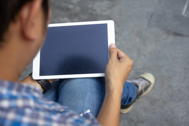 Attrappe von oben: Mann hält weißen Tablet-PC mit schwarzem leeren Desktop-Bildschirm in der Hand, während er auf dem Boden sitzt, Draufsicht. Online-Internet  - Foto, Bild