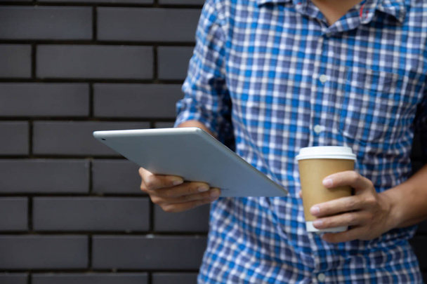 Young man using tablet computer holding coffee cup on street wall with copy space - Photo, image