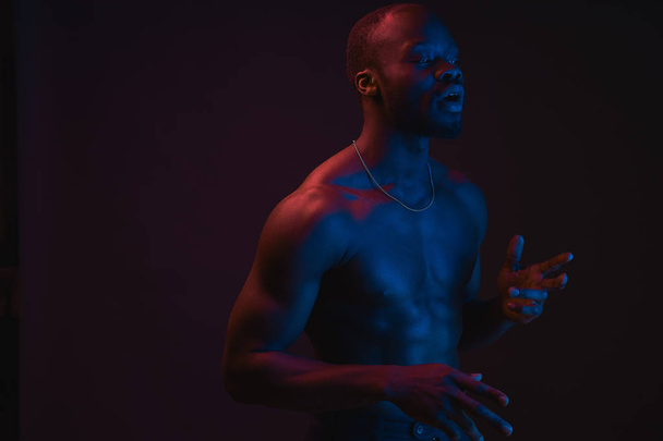 Red and blue lighted portrait of young and sexy muscular shirtless man with neck chain.  - Photo, image