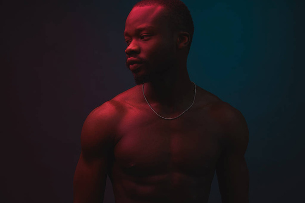 Red and blue lighted portrait of young and sexy muscular shirtless man with neck chain. Flat shadows - Foto, Bild