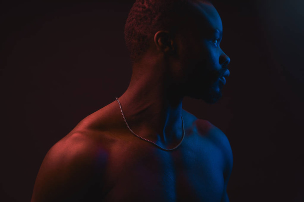 Red and blue lighted portrait of young and sexy muscular shirtless man with neck chain. Flat shadows - Fotó, kép