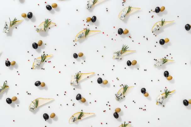 flat lay of sliced pears with blue cheese and rosemary twigs near black and green olives on white background - 写真・画像