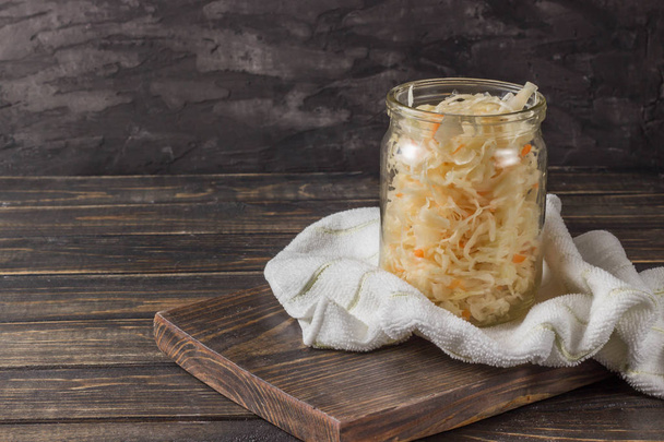 Sauerkraut en un frasco de vidrio con toalla sobre un fondo de madera oscura
 - Foto, imagen