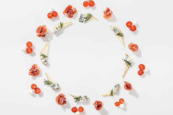 top view of sliced pears with blue cheese and rosemary twigs near tasty prosciutto, cherry tomatoes and mozzarella cheese on white background - Foto, Imagem