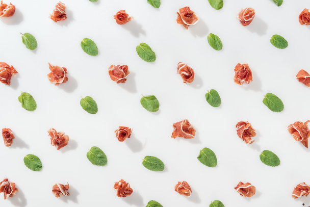 top view of delicious prosciutto near green basil leaves on white background - 写真・画像