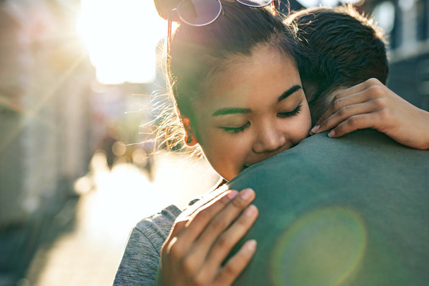 Young woman with her eyes closed hugging her boyfriend while standing together on a city street in the late afternoon - Photo, image