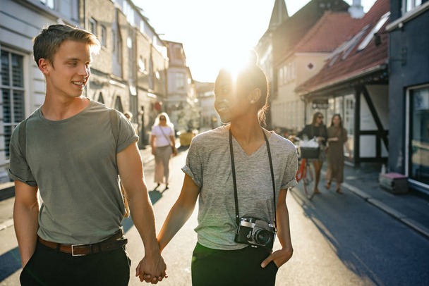 Smiling young couple talking while exploring the city streets hand in hand together in the late afternoon  - 写真・画像