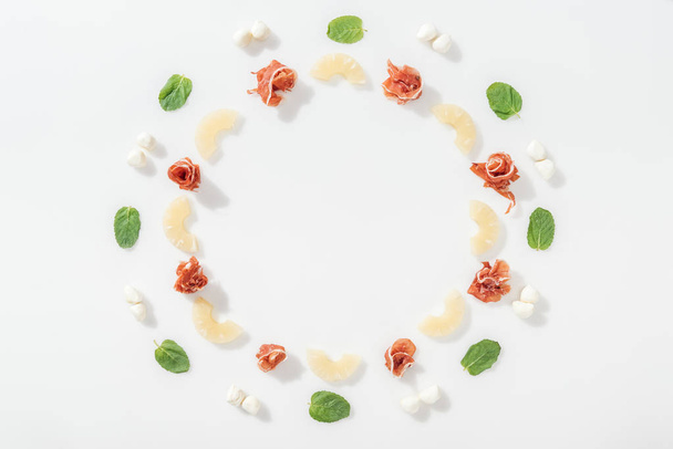 flat lay of delicious prosciutto near green basil leaves, sliced pineapples and  mozzarella cheese on white background - Photo, image