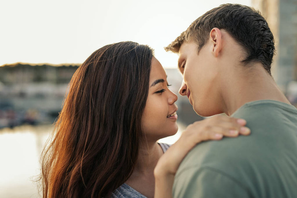 Affectionate young couple about to kiss while standing arm in arm together by a harbor in the late afternoon - Foto, Imagem