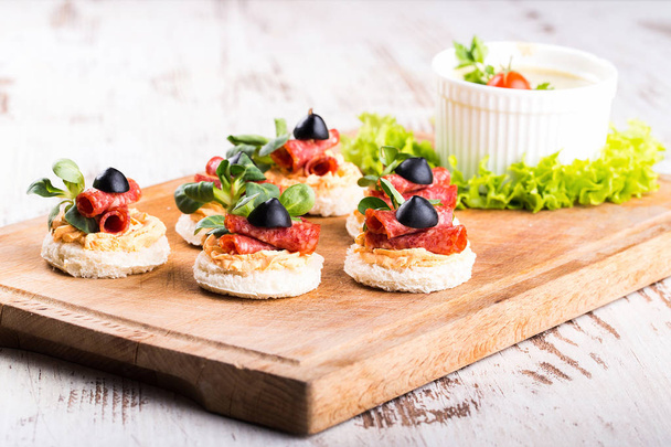 Delicious canapes with salami, olives and spices on a wooden background - Image - Photo, Image