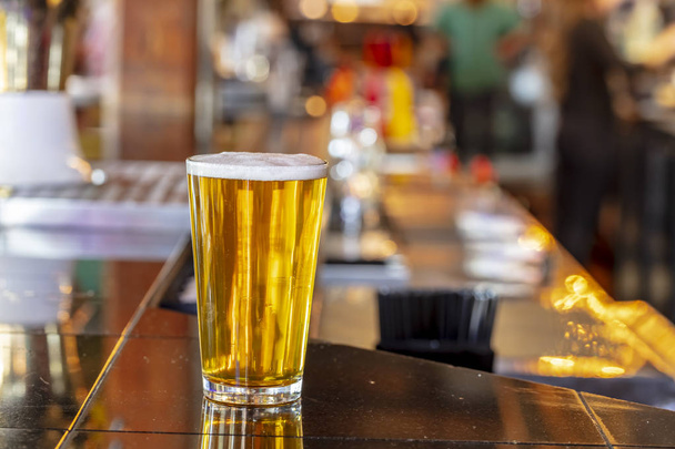 Холодное ремесленное пиво в стакане с каплями воды. Пинта пива крупным планом на фоне бара
 - Фото, изображение