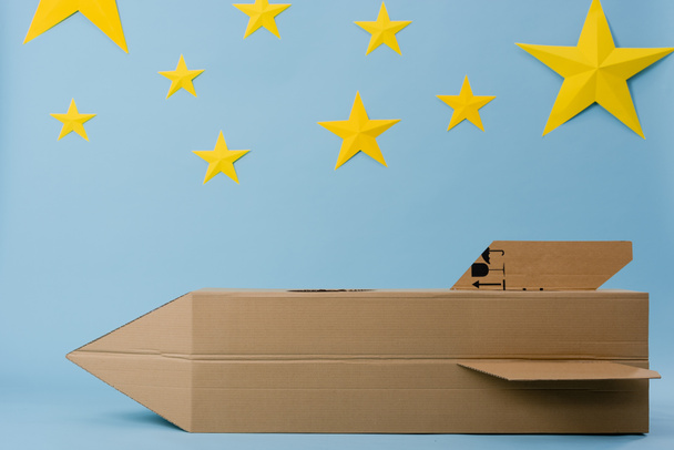 Cardboard rocket and yellow stars on blue starry background - Photo, image