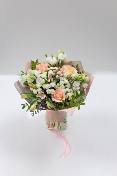 Delicate bouquet of fresh flowers (Main colors: white and pink) in a paper packaging in a vase on a light background. - Foto, immagini