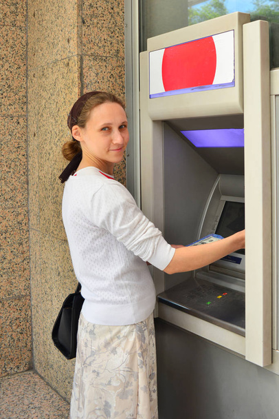 Молодий і красива дівчина стоїть біля банкомату, входить PIN-код і відмовляється гроші з картки. Концепція Фінанси та гроші. - Фото, зображення