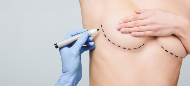 bijgesneden weergave van plastisch chirurg markering lijnen onder borst, geïsoleerd op grijs - Foto, afbeelding