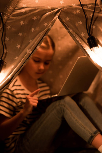 Preteen child using laptop while sitting in wigwam at home - Foto, Imagen