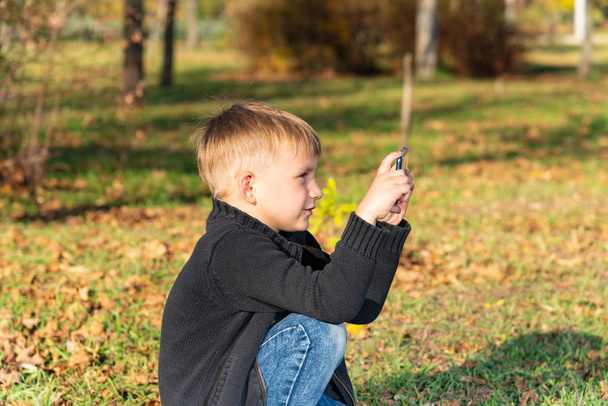 A little boy takes pictures on the phone in the park on a sunny day - Foto, immagini