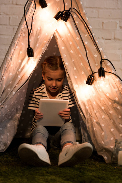 Smiling kid sitting in cozy wigwam and holding digital tablet - Photo, Image