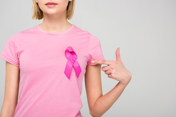 cropped view of young woman in pink t-shirt pointing at breast cancer awareness ribbon, isolated on grey - Foto, immagini