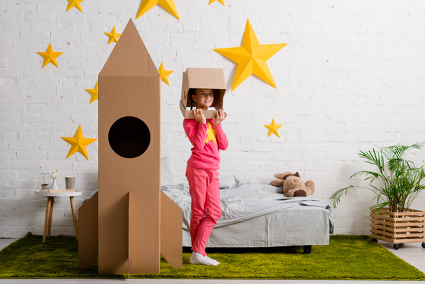 Вид в полный рост ребенка в шлеме, стоящего возле ракеты в спальне
 - Фото, изображение
