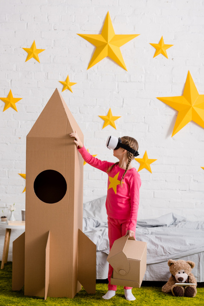 Дитина в гарнітурі vr торкається великої картонної ракети в спальні
 - Фото, зображення