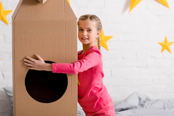 Laughing preteen kid in pink clothes holding big cardboard rocket - Foto, Bild