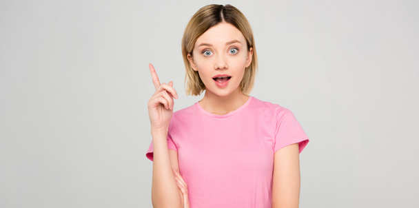 shocked beautiful girl in pink t-shirt pointing up and having idea isolated on grey - Photo, Image