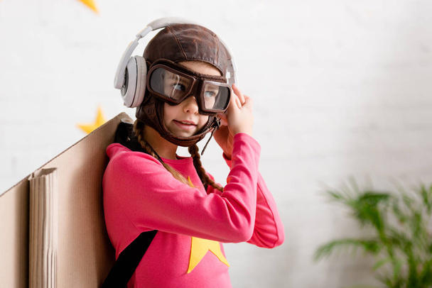 Niño en casco de vuelo y gafas escuchando música en auriculares
 - Foto, Imagen