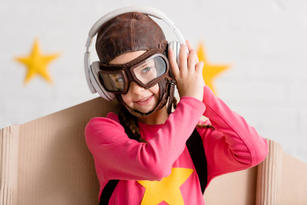 Χαμογελαστό παιδί σε πτήση κράνος και γυαλιά, ακούγοντας μουσική στα ακουστικά - Φωτογραφία, εικόνα