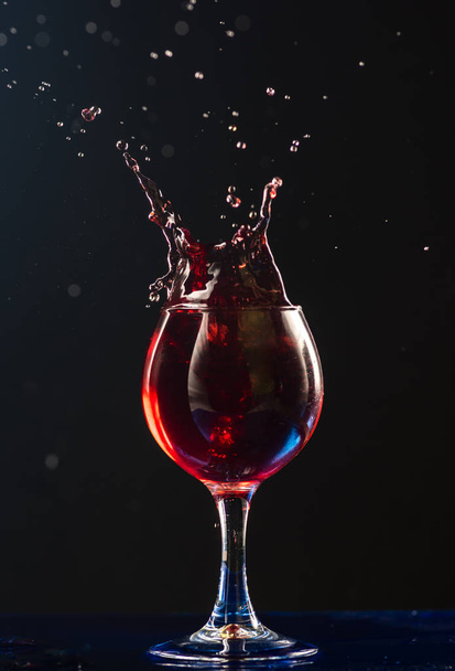 A small glass with wine on a black background and splashes nearby - Foto, Imagem