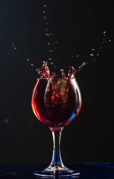 A small glass with wine on a black background and splashes nearby - Foto, Imagem