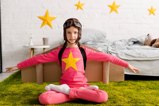 Niño inspirado en casco de vuelo sentado en pose de loto en la alfombra
 - Foto, Imagen