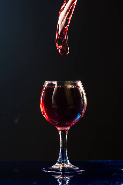 A small glass with wine on a black background and splashes nearby - Zdjęcie, obraz