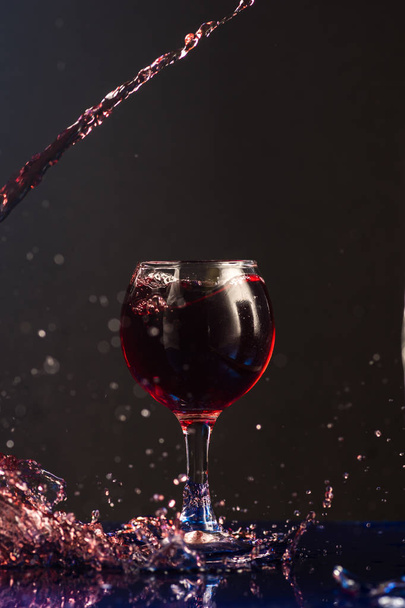 A small glass with wine on a black background and splashes nearby - Zdjęcie, obraz