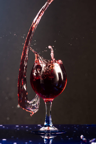 A small glass with wine on a black background and splashes nearby - Φωτογραφία, εικόνα
