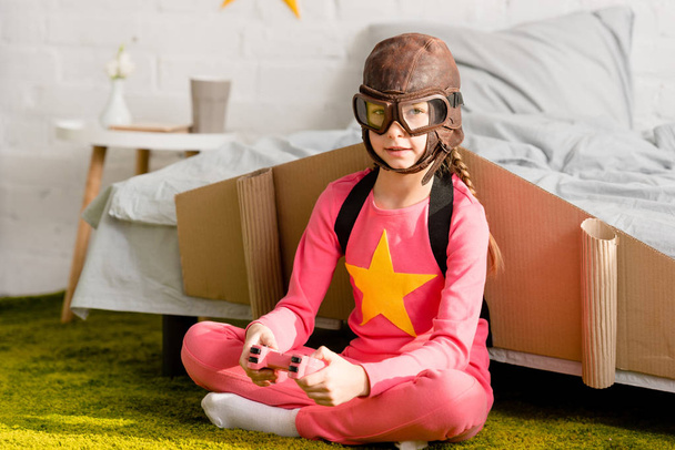 Bambino in volo casco seduto su moquette con gamepad
 - Foto, immagini