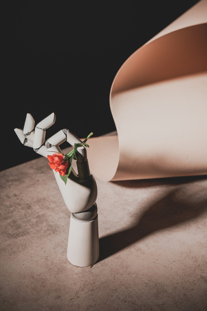 pink rose flower in robotic hand on stone table with sheet of paper isolated on black - Photo, Image