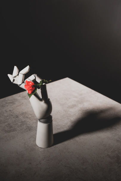 pink rose flower in robotic hand on stone table on black background - Fotó, kép