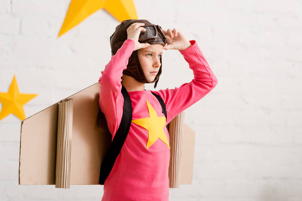 Confident child with cardboard wings touching goggles - 写真・画像