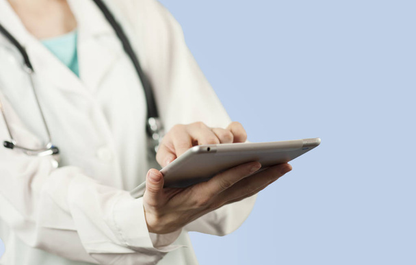 eine junge schöne Ärztin mit einem Computer in der Hand sucht nach Informationen auf blauem, isoliertem Hintergrund. das Konzept der Gesundheit und moderne medizinische Netzwerktechnologien - Foto, Bild