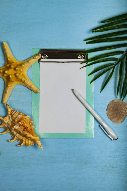 Planning a trip to the sea. Paper,seashells, starfish and leaf of palm tree on a blue wooden background. - 写真・画像