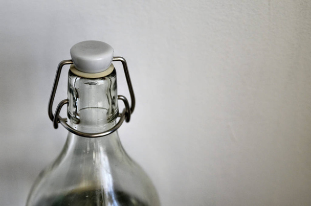 Прозрачная стеклянная бутылка на нейтральном белом фоне. Полный воды, механизм закрытия с прокладкой и крышкой
. - Фото, изображение