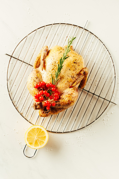 top view of fried chicken, rosemary and berries on metal grille with lemon - Фото, изображение