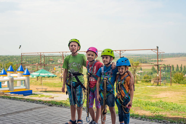 Quatro crianças estão usando capacetes e roupas de escalada e estão prontas para superar obstáculos em um parque extremo
 - Foto, Imagem