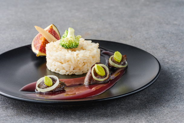 riso, broccoli, fichi e carne fritta con salsa su piatto nero e superficie in pietra
  - Foto, immagini